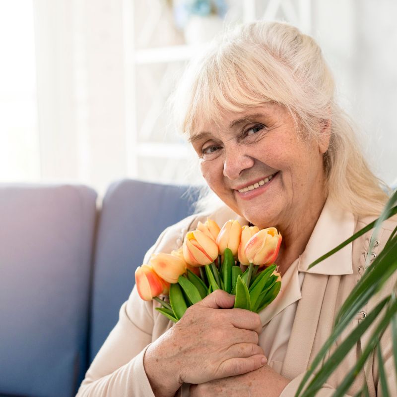 Seniorin glücklich mit ihrem Pflegedienst, lächelt mit Blumen in ihrer Hand